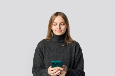 Gri arka planda izole edilmiş cep telefonu kullanırken gülümseyen genç sarışın kadın. Yüksek kalite fotoğraf