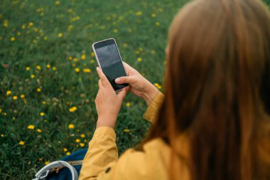 Genç bir kadının cep telefonuna dokunduğunu ve çayırda oturduğunu gördüm. Yüksek kalite fotoğraf