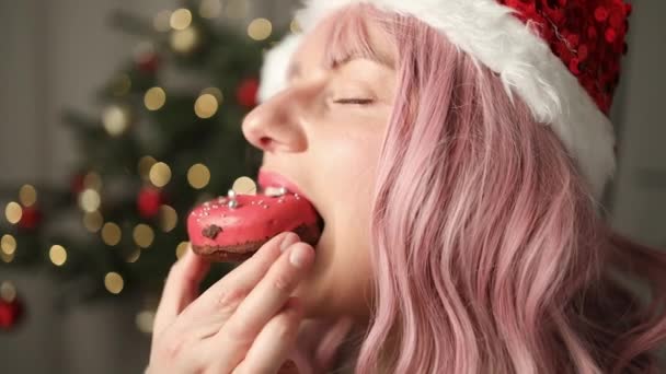 Щаслива Жінка Кусає Пончик Десерт Виглядає Камерою Фоні Різдвяних Вогнів — стокове відео