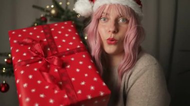 Neşeli, pembe saçlı, elinde hediyeyle kameraya bakan neşeli ve mutlu yüzlü bir kadın. Yüksek kaliteli FullHD görüntüler