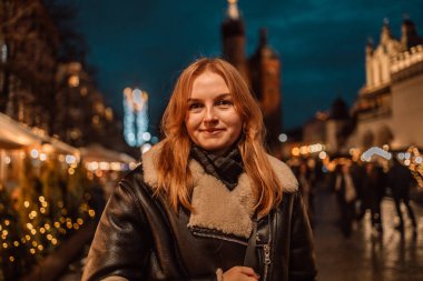 Gülümseyen güzel bir kadın mutlu bir şekilde Xmas caddesinde duruyor ve Polonya 'nın Krakow kentindeki kasaba meydanındaki Noel pazarında kameraya bakıyor. Kış tatili ve kutlama konsepti. Yüksek kalite