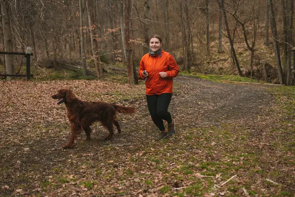 Sağlıklı, aktif bir yaşam tarzı konseptiyle, evcil köpeğiyle birlikte arka planda koşan mutlu şişman kadın. Yüksek kalite fotoğraf