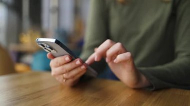 Kahve dükkanında kahve masasında otururken elinde akıllı telefon tutan ve cep telefonunu kaydıran bir kadının görüntüsü. Çalışan insanlar pazarlama işiyle, teknolojiyle iletişime geçiyor. Yüksek kalite FullHD