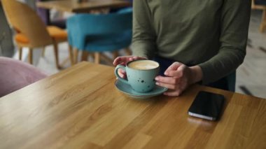 Genç ve güzel bir kadın bir kafede cappuccino içiyor. Nefis bir kahvaltı. Kadınların elleri bir fincan kahve tutar..