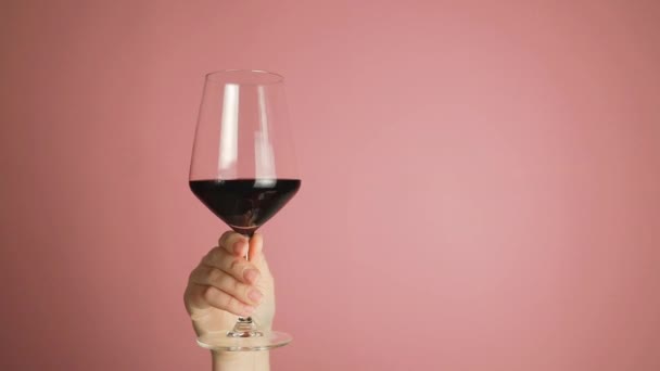 ワイングラスで赤ワインを泳ぐ女性の手を閉じます ピンクの壁のスタジオの背景にあるワインのテイスティング 飲料ワイン 高品質のフルHd映像 — ストック動画