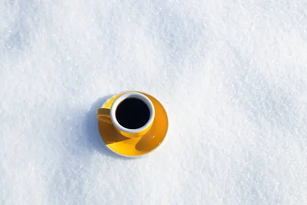 Winter background. Yellow cup with hot coffee or tea stand on the snow outdoor at sunny day with cold weather outdoors.