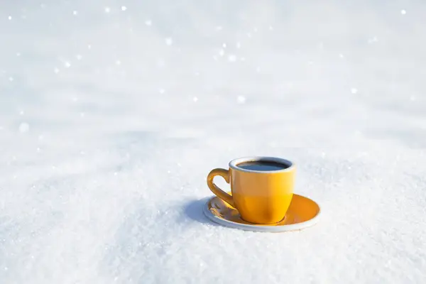 Winter background. Yellow cup with hot coffee or tea stand on the snow outdoor at sunny day with cold weather outdoors.
