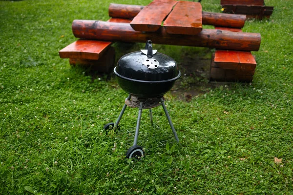 Side view of black barbecue grill with cover in a front of house or backyard and green lawn. Portable barbecue grill for outdoor cooking.