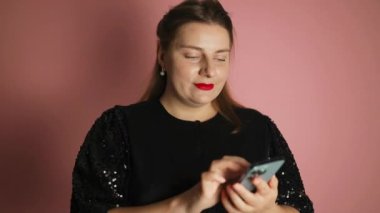 Siyah elbiseli gülümseyen genç bir kadın yılbaşı Noel tatilinde evde akıllı telefon kullanıyor. Kız bir tebrik mesajı yazıyor, arkadaşlarıyla sohbet ediyor ya da internetten alışveriş yapıyor. Yüksek kalite