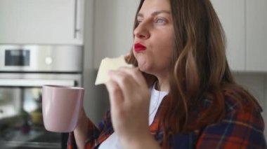 Elinde fincanla sıcak çay ya da kahve tutan güzel bir kadının portresi. Çekici genç bir bayan öğle yemeğinde sandviç yiyor. Kötü beslenme. Kötü alışkanlık. Yüksek kaliteli FullHD görüntüler