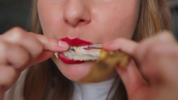 视频中的女性穿着红色口红的白色T恤 吃着炸鸡 在舒适的家的厨房里吃着坚果 — 图库视频影像