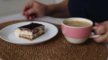 Kafkasyalı 60 'lı yaşlardaki kadının pencerenin kenarında oturup kahve ya da mutfakta çay içmesini yakın çekim. Güzel bir kadın kahve içmekten ve tiramisu pastası yemekten hoşlanır. İtalyan peynirli kekinden bir ısırık alıyorum.