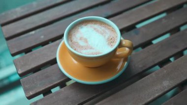 Sarı latte ya da cappuccino kahve bardağını dijital tablette tahtaya, balkondaki pencereye yakın çekim. Beyaz fincanda buharlı sabah kahvesi. Yüksek kaliteli FullHD görüntüler