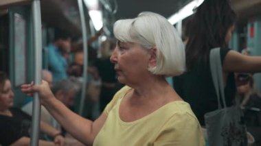 60 'lı yaşlarda Avrupalı bir kadın toplu taşımada duruyor. Modern tramvaydaki toplu taşımacılıkta geziden zevk alan güzel bir kadın. Yüksek kaliteli FullHD görüntüler