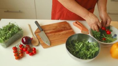 Kadın ev mutfağında lezzetli ve sağlıklı bir öğle yemeği hazırlıyor. Kadın ellerinin, tahta tahtada bıçakla taze bir domatesi keserken yakın plan çekimleri.. 