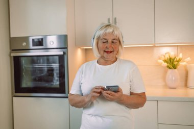 60 'ların mutlu kadını mutfakta cep telefonu kullanıyor. Yüksek kalite fotoğraf