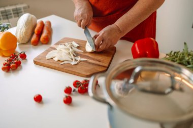 Kadın aşçı taze soğanları tahtada dilimlerken İtalyan makarnasını sebzeli ve çorbalı hazırlıyor.