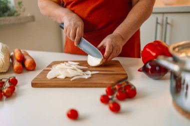 Kadın aşçı taze soğanları tahtada dilimlerken İtalyan makarnasını sebzeli ve çorbalı hazırlıyor.