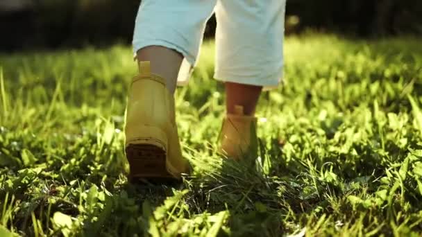 黄色いゴム製ブーツのガーデナー女性の足は 緑の草と瓦礫の土地の道路の地面を歩いています 秋のシーズン クローズアップ — ストック動画