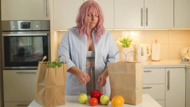 キッチンに立っている白人太った女性 新鮮な野菜を取り出してテーブルに置く女性アンパック リンゴのスニッフィング野菜 トークフード配信 オンライン — ストック動画