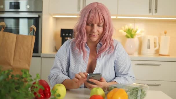 オンラインで注文する食品 キッチンで調理しながら インターネットから食料品の配達を購入する携帯電話を持つ笑顔の白人女性 高品質のフルHd映像 — ストック動画
