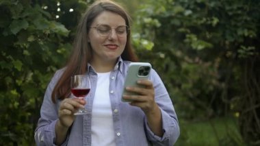 Dışarıda telefonuyla bir kadeh şarap içen neşeli beyaz bir kadının portresi..