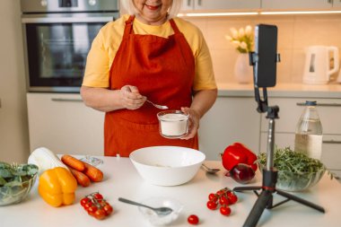 Kafkasyalı bir kadın, vejetaryen salata yemeği pişirirken video blogunda yemek tarifi ararken akıllı telefon kullanıyor. Gıda vlog kaydedicisi bir video kaydediyor