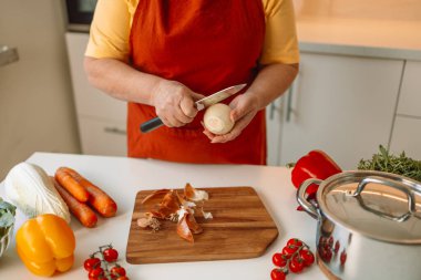 Kadın aşçı taze soğanları tahtada dilimlerken İtalyan makarnasını sebzeli ve çorbalı hazırlıyor.