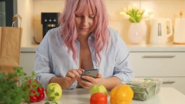 İnternetten yemek sipariş ediyorum. Mutfakta yemek pişirirken internetten alışveriş yapan gülümseyen beyaz kadın. Yüksek kaliteli FullHD görüntüler