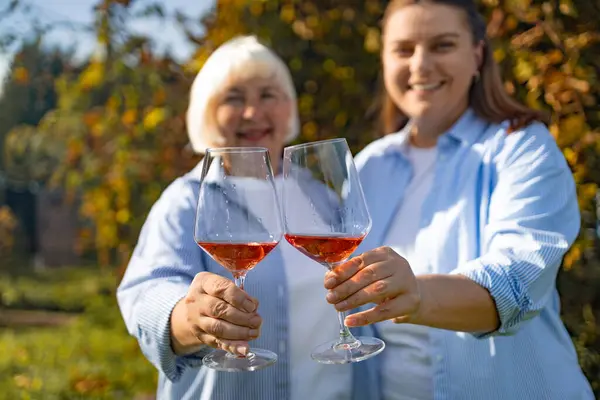 Two women of different ages are celebrating something at backyard at garden. Pretty middle aged woman and her adult daughter drinking wine at summer day. High quality photo