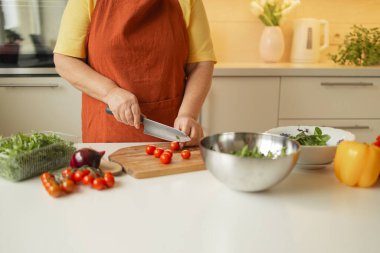 Kadın aşçı, mutfakta sebzeli İtalyan salatası hazırlarken tahtada taze vişneli domates dilimliyor.