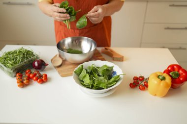 Elinde bıçak ve taze ıspanak tutan 60 'lı yılların son sınıf sarışın beyaz kadın kırsal mutfağında bir kase sağlıklı diyet salatası hazırlıyor. Yüksek kalite fotoğraf