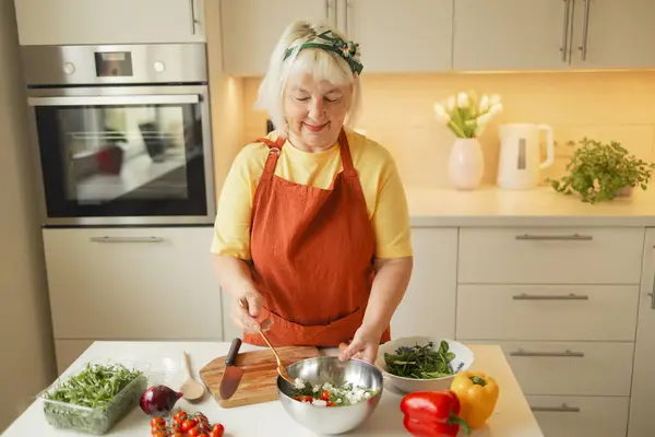 Close up of senior woman is preparing vegetable salad in the kitchen.Female adding arugula to salad. Healthy Food. Vegan Salad. Diet. Dieting Concept. Healthy Lifestyle. Cooking At Home. Prepare Food