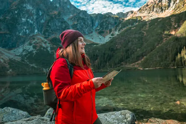 Shot of lost woman traveler with map and backpack relaxing outdoor with rocky on Morskie Oko lake. Woman traveler explorer with backpack hiking to the top of the mountain. Hiking travel and adventure