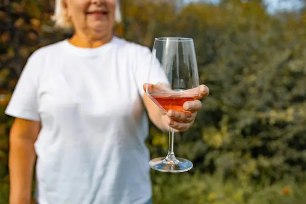 Hand holding a glass of pink wine on the blurred background at backyard, having fun outdoors in the evening.