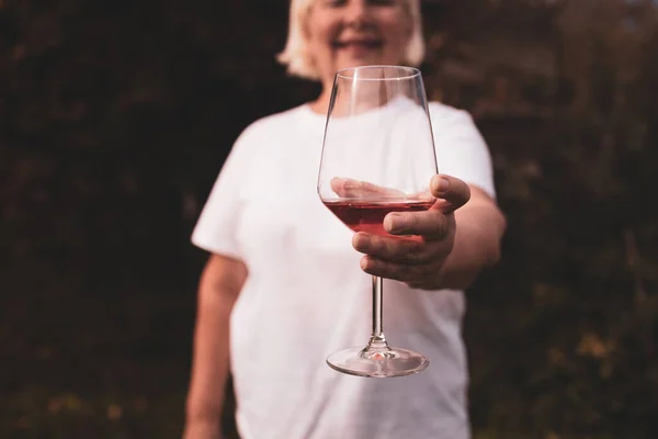 Hand holding a glass of pink wine on the blurred background at backyard, having fun outdoors in the evening.