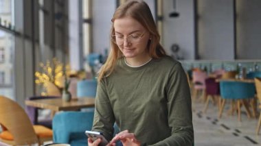 Kafede kahve içerken cep telefonu kullanan mutlu güzel bir kız. Cep telefonu tutan ve akıllı telefona bakan 30 'lu yaşlardaki güzel sarışın bir kız. Yüksek kaliteli FullHD görüntüler