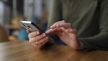 Kadın bir kafede dinleniyor ve yüksek kaliteli FullHD kamera görüntülerinin tadını çıkarırken bir masada akıllı telefonunu kullanıyor.