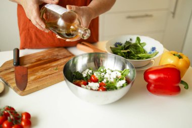Kadın mutfakta yemek hazırlarken sebze salatası hazırlıyor. Tanınmayan şef evde vejetaryen yemeği hazırlarken zeytinyağı ekliyor. Sağlıklı yeme kavramı. 