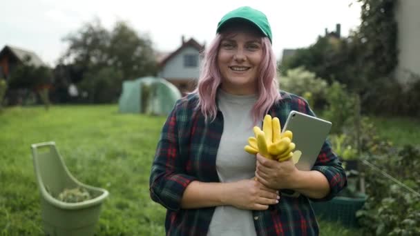 ハッピーコーカサス州の女性は 仕事の服を着て 裏庭の庭で働いている間 カメラの前で笑顔のタブレットでゴム手袋を保持しています 高品質のフルHd映像 — ストック動画