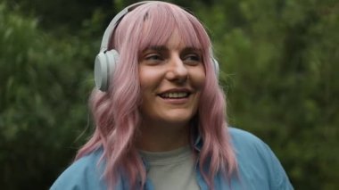 Uzaktan kumandalı beyaz kulaklık takan hoş bir bayan. Keyfi yerinde ve arka bahçede dans ediyor. Mavi gömlekli bir kadın elleriyle dalgalar yaratıyor ve müzik dinliyor..