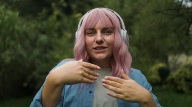 Uzaktan kumandalı beyaz kulaklık takan hoş bir bayan. Keyfi yerinde ve arka bahçede dans ediyor. Mavi gömlekli bir kadın elleriyle dalgalar yaratıyor ve müzik dinliyor..