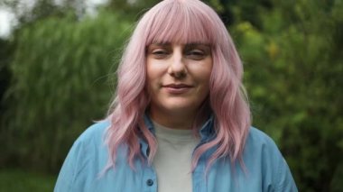 Şirin pembe saçlı bayanın yaz bahçesindeki kameraya gülümseyişinin yakın fotoğrafını çek. Yüksek kaliteli FullHD görüntüler