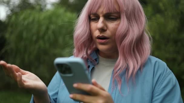 神経質な不幸な若い白人ピンクの髪の女性の肖像画は 市街地で彼女の携帯電話にメッセージを送ったときにイライラします アウトドアでスマートフォンが問題を抱えている女性をノイズ — ストック動画