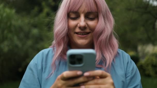快乐的粉红头发姑娘慢动作地在电话里读好消息 喜形于色的女孩在网上庆祝胜利 用智能手机阅读好消息 感到惊奇 优质Fullhd影片 — 图库视频影像