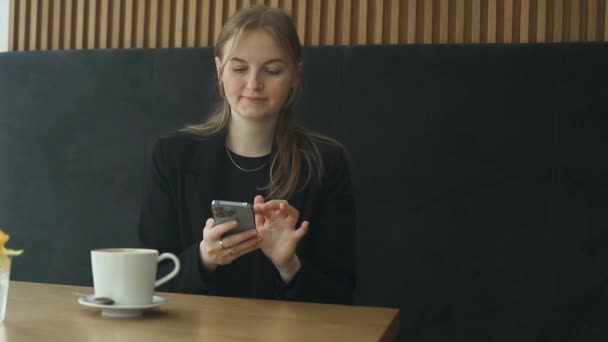 年轻快乐的女商人30多岁穿着西服 拿着手机聊天 拿着杯子喝茶 一个人坐在咖啡店餐厅的桌子旁 自由职业办公室业务的概念 — 图库视频影像