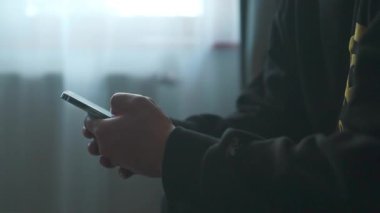 Modern tasarım dizaynında koltukta otururken akıllı telefon kullanan erkek elleri sosyal ağda SMS mesajı yazan neşeli hippi adam. Yüksek kaliteli FullHD görüntüler