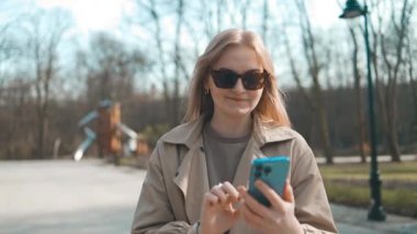 Ofisin yanında dikilen, sıradan giyinmiş, gülümseyen iş kadını. Elinde cep telefonu olan bir iş kadını kameraya bakıyor. Yüksek kaliteli FullHD görüntüler