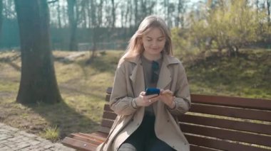 Gülümseyen gözlüklü iş kadını Central City caddesinde yürüyor ve bir alışveriş merkezinin arka planında telefonunu kullanıyor..