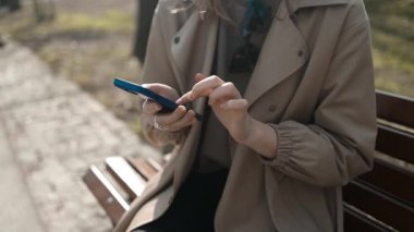 Gülümseyen gözlüklü iş kadını Central City caddesinde yürüyor ve bir alışveriş merkezinin arka planında telefonunu kullanıyor..